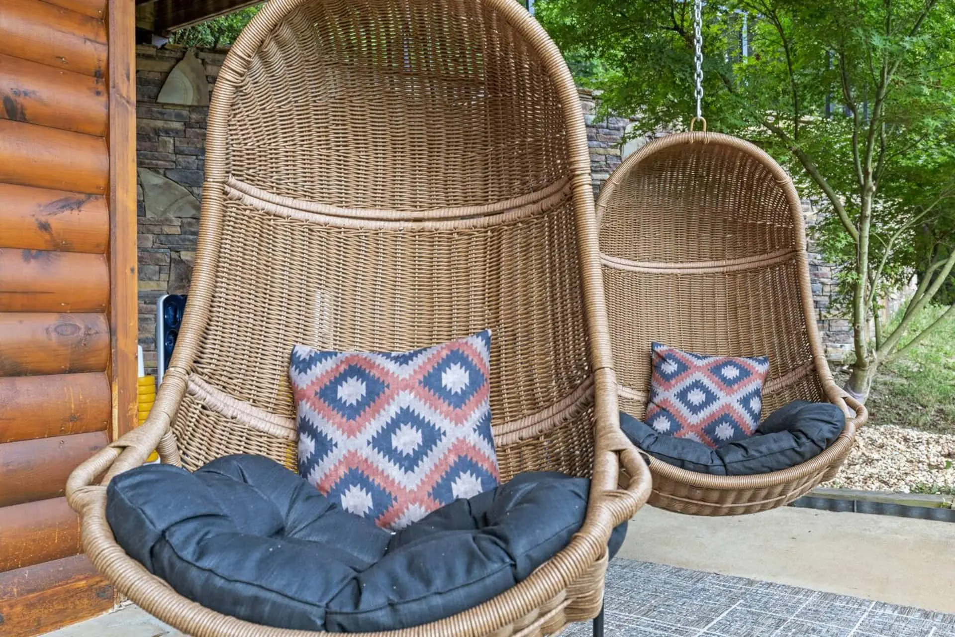 Unwind in cozy hanging wicker chairs on the covered patio, complete with plush cushions and stylish pillows—perfect for relaxing after the hot tub while enjoying peaceful views of the surrounding trees.