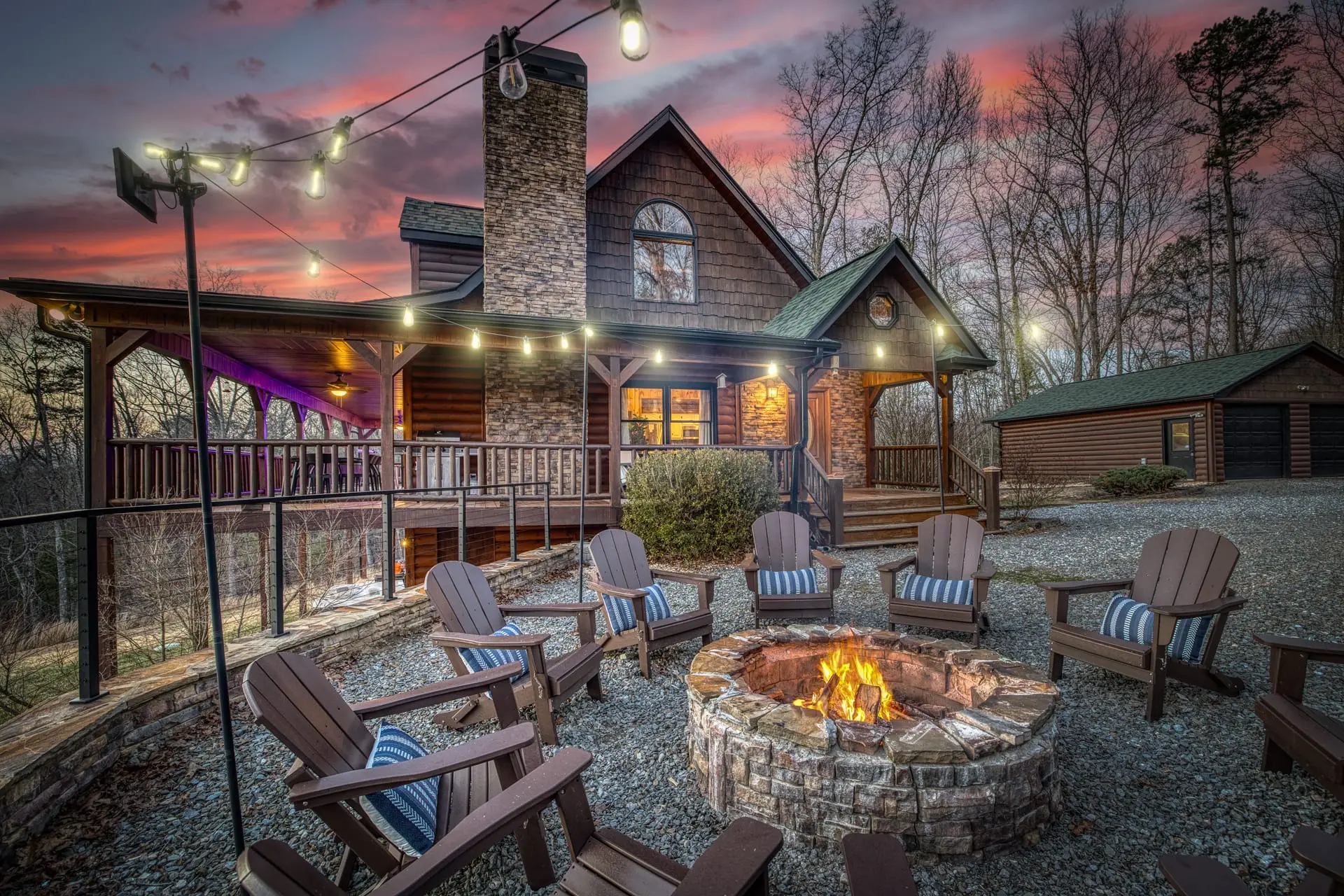Twilight fire pit gathering space with cozy Adirondack seating and glowing string lights, set in front of the rustic cabin and covered porch—perfect for relaxing evenings under the Blue Ridge mountain sky.