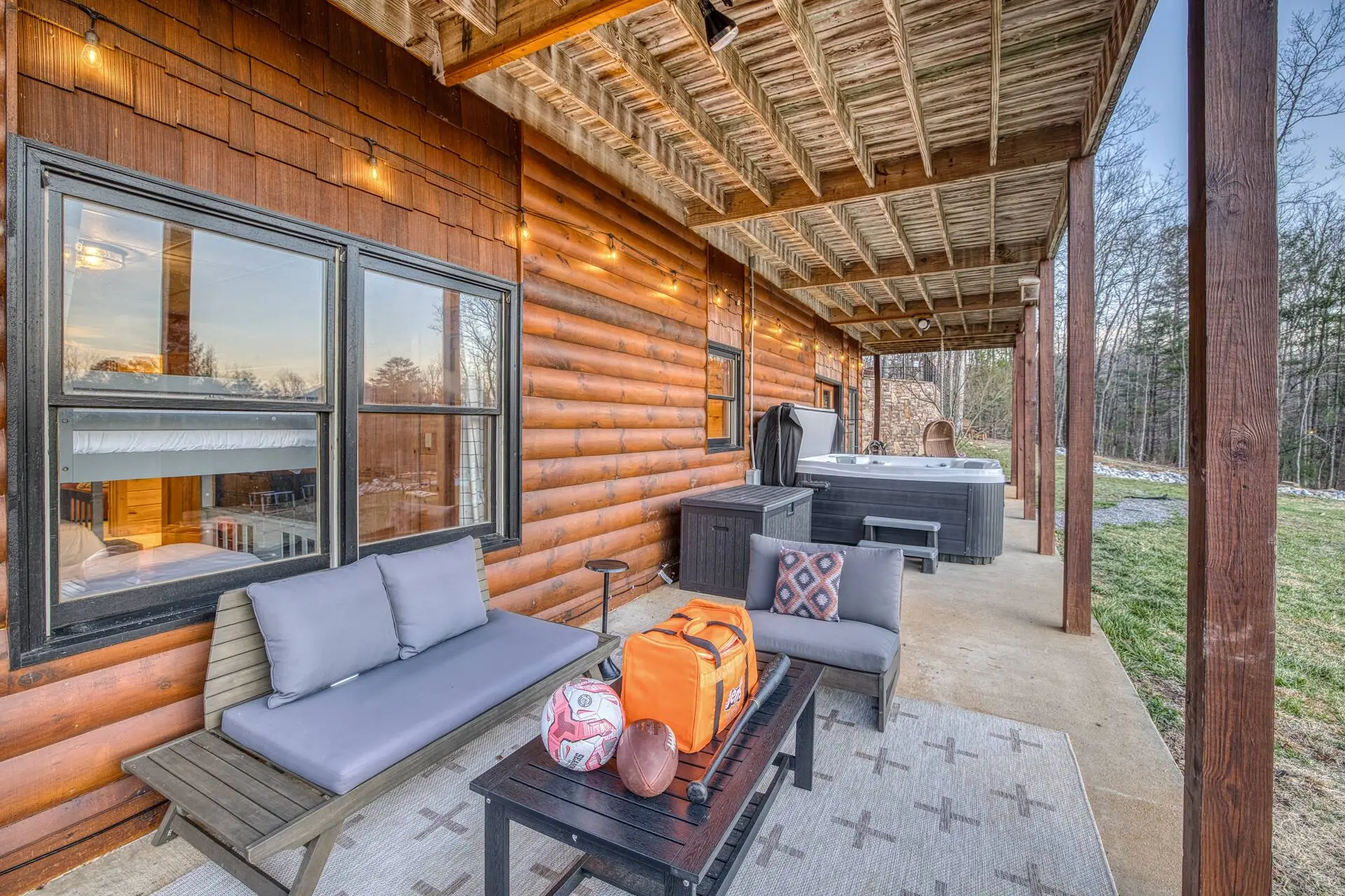 Cozy covered cabin patio with hot tub, lounge seating & forest views